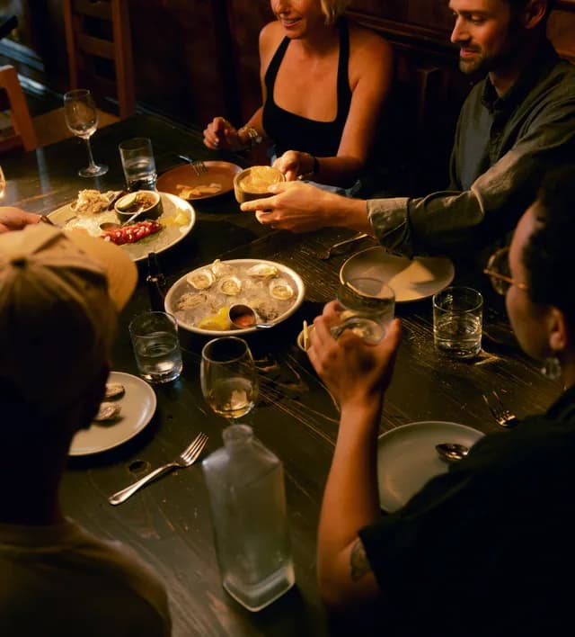 Friends passing dishes around a dinner table lit from above